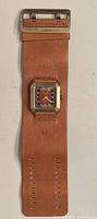 Full view of the men's Nixon leather watch showing wide tan leather cuff strap and bronze square case with brown dial.