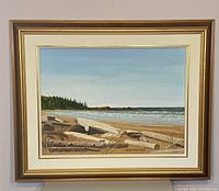 Framed oil painting showing a beach scene including sand, driftwood, trees, and ocean waves under a clear sky.