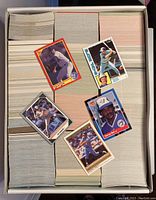 Photo of a large box filled with thousands of baseball cards from 1980s and early 90s, with five individual cards laid on top for sample.