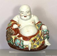 Front view of seated vintage Chinese Buddha statue showing smiling face, exposed belly, and detailed famille rose robe with floral and geometric designs.