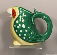 Side profile of the ceramic parrot jug showing green wings with white dots and a handle shaped as part of the tail.