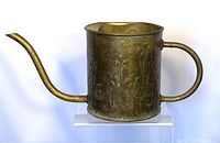 Side view of vintage brass watering can showing curved handle and slender spout with slight looseness.