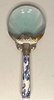 Full view of the magnifying glass showing clear large round lens and porcelain handle with blue floral pattern.