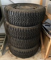Stack of four black winter tires mounted on steel rims.