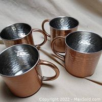 Four copper mugs arranged with visible hammered texture and metal lined interiors.