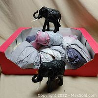 Box containing seven wrapped elephant figurines with one unwrapped black carved elephant figurine on top and another in front.