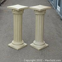 Pair of cream-colored Roman style fluted pillars with square bases and tops, shown outdoors on pavement.