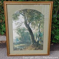 Framed print showing a tree beside a pond with dense foliage and broad leaves, in an arched window mat and gold-tone frame.