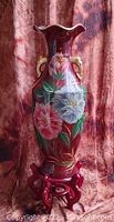 Front view of a tall Asian floor vase with red background and hand-painted floral decorations in pink, white, and green, with ornamental handles and scalloped rim.