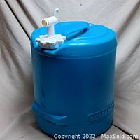 Blue water container with white spigot and screw-on cap, side view showing handle and spigot