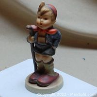 Front view of the Hummel figurine showing the child with a walking stick, dressed in hiking outfit with cap and scarf.