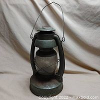 Full front view of the antique metal railroad lantern showing the wire handle, round glass globe, and base.