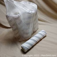 Set of 12 white and black striped paint rollers in sealed plastic package with one roller outside placed on a beige fabric.