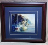 Framed boat print showing sailboats near rocky shore with navy blue matting and dark wood frame