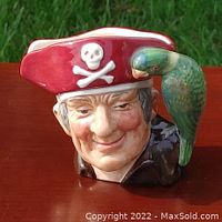 Close-up front view of Royal Doulton Long John Silver character jug in red hat with parrot on shoulder, showing detailed facial features and bright colors.