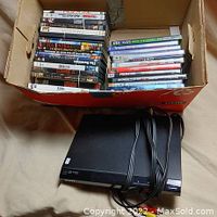 Box containing a variety of DVDs with some movie titles visible and a Sony DVD player underneath with attached cables.