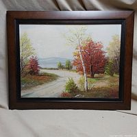 Full view of the framed landscape oil painting depicting a country path with autumn trees and water in the background.