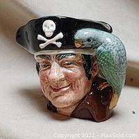 Close-up of the ceramic jug depicting Long John Silver with his pirate hat and a green parrot on his shoulder, showing facial details and skull emblem on the hat.