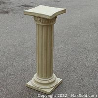 Front-facing photo of a beige decorative classical column pedestal with vertical fluted grooves, square base, and curved square top