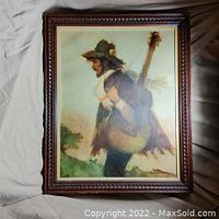 Framed painting of a travelling musician carrying a guitar, showing the detailed wooden frame and artwork.