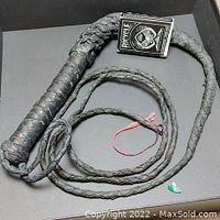 Black braided 8-foot leather whip coiled with tightly wrapped handle next to Bicycle playing cards deck.