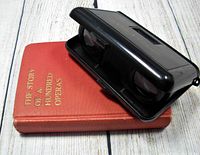 Photo showing the red hardcover book 'The Story of a Hundred Operas' along with vintage folding opera glasses resting on top.