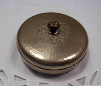 Closed view of the circular metal covered dish showing hammered texture lid with embossed cherry blossom design and floral knob