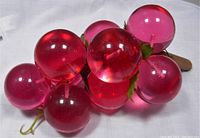 Pink and red translucent Lucite spheres arranged to resemble a bunch of grapes with artificial leaves and wooden stem