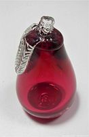 Oblique side view showing the cranberry red glass pear with clear glass stem and leaf detail on top.