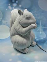 White ceramic squirrel lamp unlit, showing shape and details of the squirrel holding a nut.