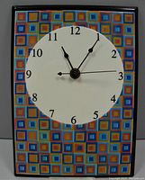 Front view of the handpainted ceramic wall clock showing the multicolored square pattern border and white face with black numbers and hands.