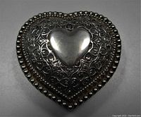 Top view of heart shaped trinket box showing smooth raised heart center with ornate scrolling and bead border.