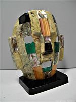 Front right angle showing detailed semi-precious stone mosaic patchwork on mask and black base
