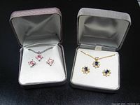 Two boxed sets of costume jewelry, each including a necklace and matching earrings; one set silver-tone with pink stones, the other gold-tone with blue stones
