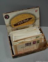 Open vintage 'Peg Top' cigar box filled with many envelopes, packets, and loose postal covers containing a large variety of old stamps.