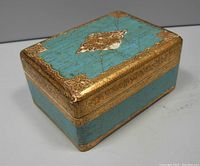Top and side exterior view of the rectangular turquoise and gold music box with decorative patterns.