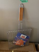 Single BBQ grill basket with metal wire grid and wooden handle, 11x11 inch size labels visible.
