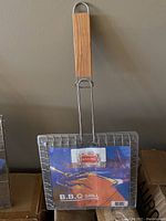 Front view of a BBQ grill basket showing packaging label and wooden handle