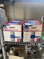 Six boxed units of Bialetti Colorama coffee makers on metal shelving.