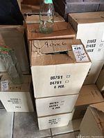 Stack of cardboard boxes each containing 6 glass bottles, labeled with product codes and fragile markings.