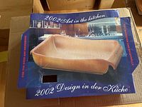 Photo showing the front of the box with image of ceramic rectangular baking dish labeled '2002 Design in der Küche'.