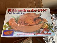 Box top showing image of ceramic chicken-shaped baking dish with roasted chicken inside, labeled Hähnchenbräter Chicken-Baker.