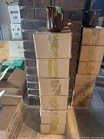 Six stacked cardboard boxes sealed with tape, each containing ceramic pitchers, brown pitcher placed on top for display.