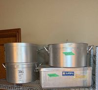 Four Metalco commercial heavy gauge aluminum pots and lids on one shelf, sizes noted on green tape.