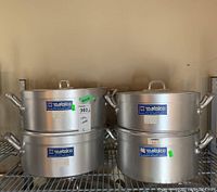 Four heavy gauge aluminum sauce pans with handles and lids arranged on shelving, showing brand and size labels.