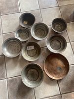 All nine copper bowls and tray displayed on tiled floor, showing different sizes and patina.