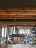 Photo showing a large copper hanging planter suspended by brass chains in a room with visible kitchen cabinets and shelving.