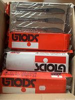 Box with multiple Sciola branded orange and white boxes containing serrated stainless steel knives in plastic wrapping.