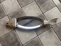 Full view of the fish-shaped stainless steel platter on tiled floor showing overall shape and size.