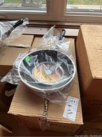 Two enamel Teflon coated frying pans in plastic wrappers on cardboard boxes, showing black handles and the brand label inside the pans.